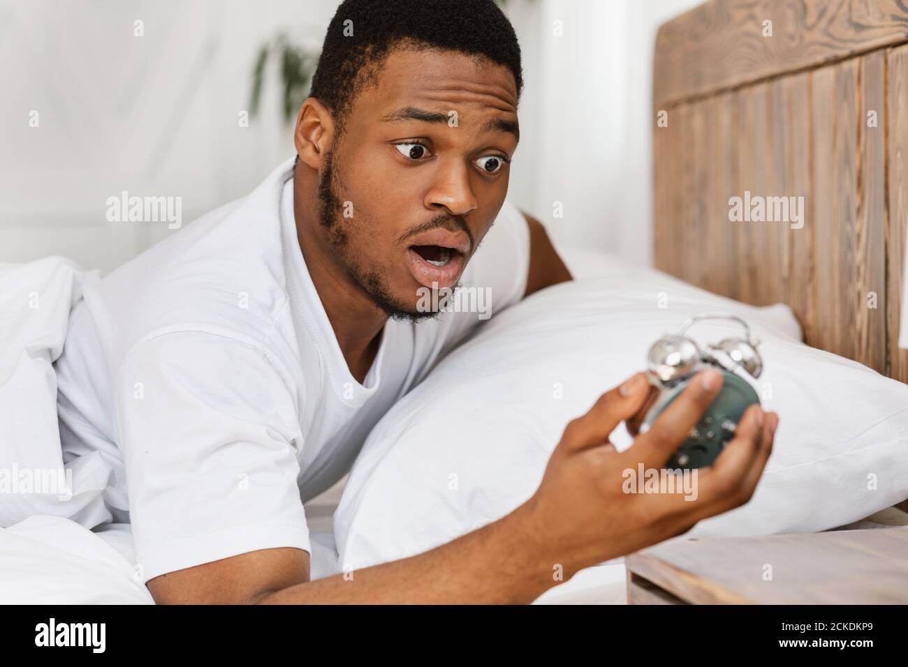 Overslept African Man Holding sveglia svegliarsi nel letto interno Foto Stock