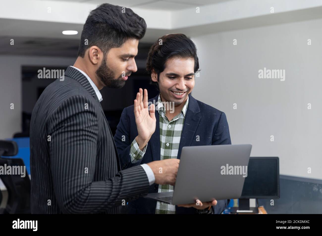 Ritratto di due giovani bei uomini d'affari indiani che agitano mano al laptop, videoconferenza con il cliente, discutere di progetto, ambiente aziendale. Foto Stock