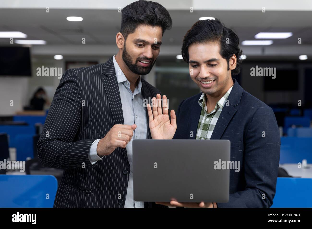 Ritratto di due giovani bei uomini d'affari indiani che agitano mano al laptop, videoconferenza con il cliente, discutere di progetto, ambiente aziendale. Foto Stock