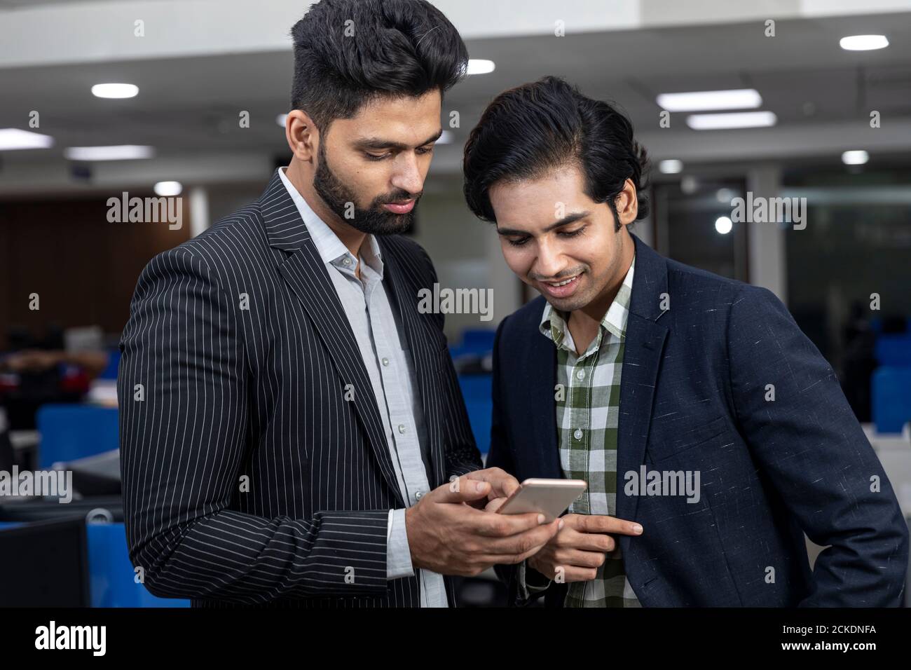 Ritratto di due giovani bei uomini d'affari indiani che guardano al telefono, discutono progetto, ambiente aziendale. Foto Stock