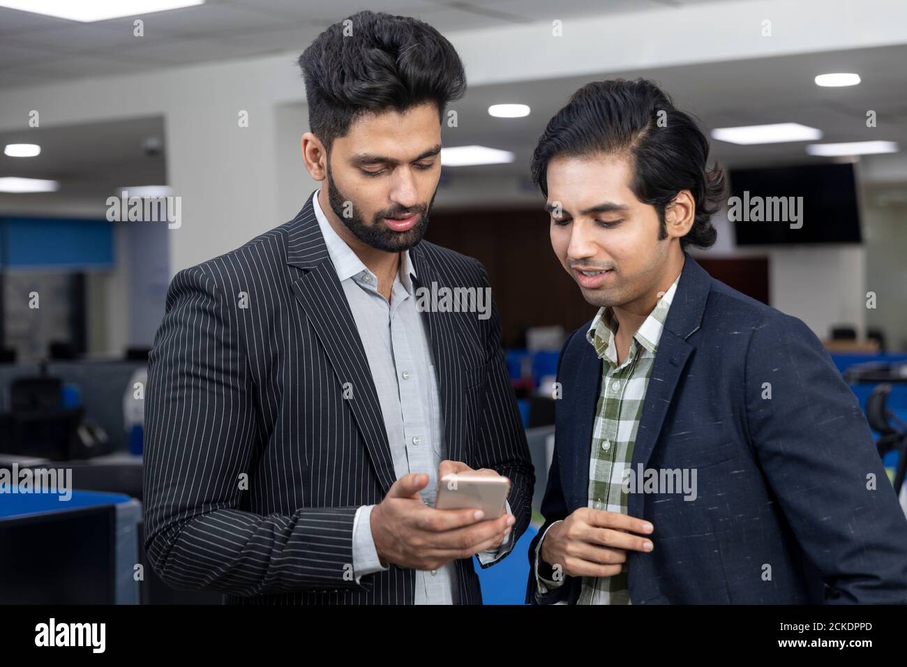 Ritratto di due giovani bei uomini d'affari indiani che guardano al telefono, discutono progetto, ambiente aziendale. Foto Stock
