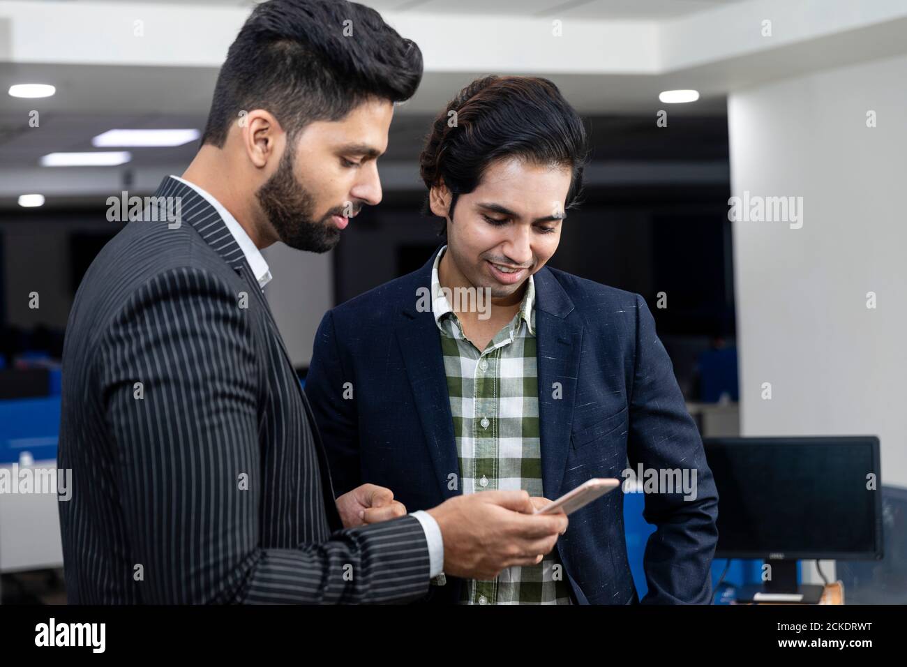 Ritratto di due giovani bei uomini d'affari indiani che guardano al telefono, discutono progetto, ambiente aziendale. Foto Stock
