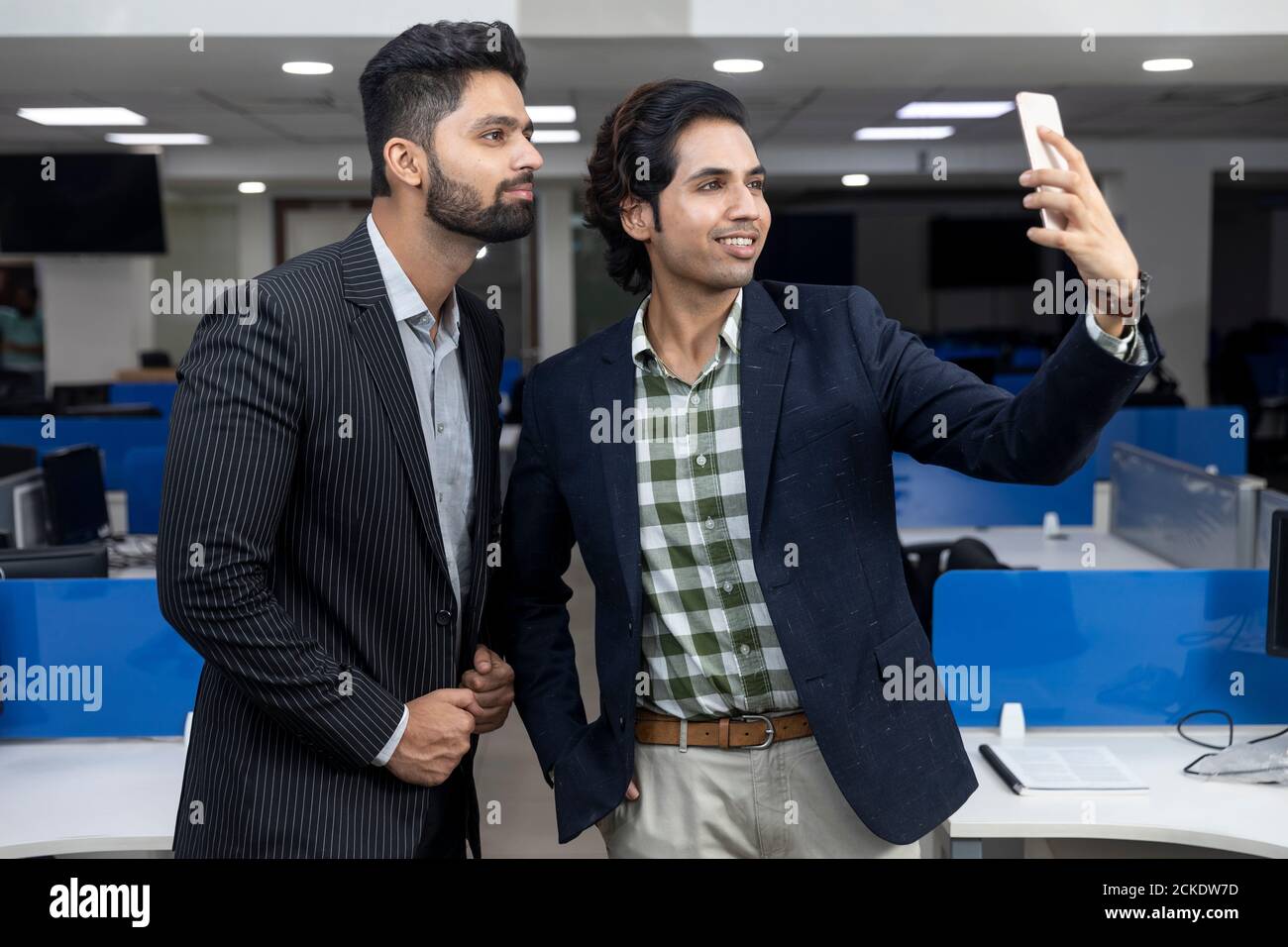 Ritratto di due giovani bei imprenditori indiani che guardano al telefono, videoconferenza con il cliente, prendendo selfie, discutendo progetto, Foto Stock