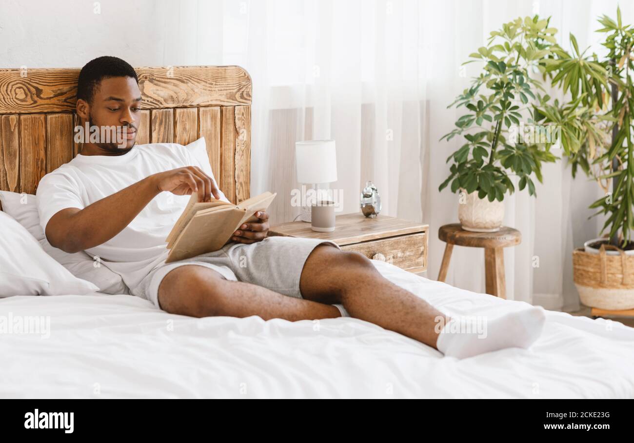 Libro di lettura dell'uomo Africano Americano che si trova nel letto a casa Foto Stock