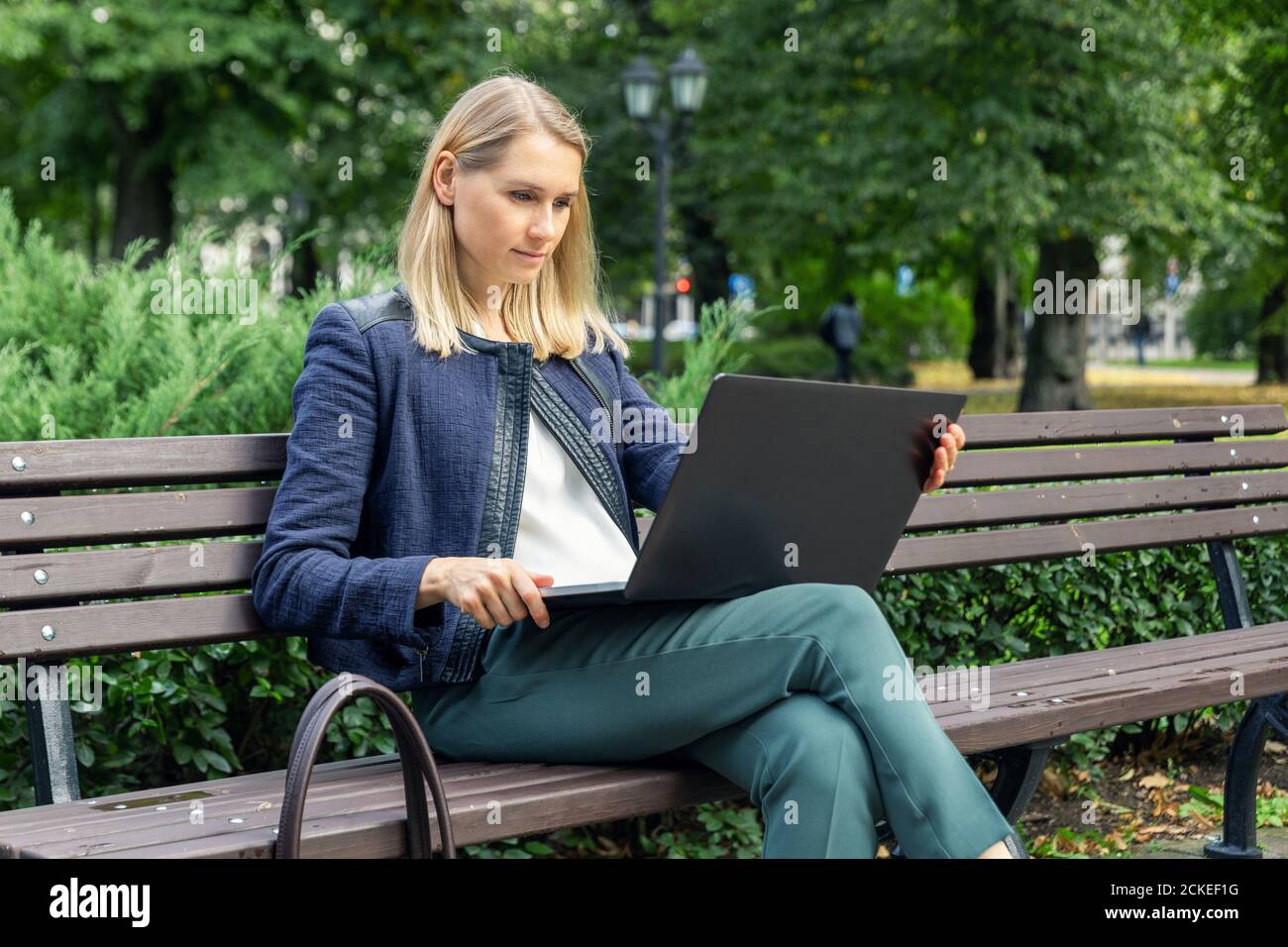 giovane e attraente donna d'affari seduto sulla panchina del parco cittadino e utilizzando un computer portatile. ufficio esterno Foto Stock