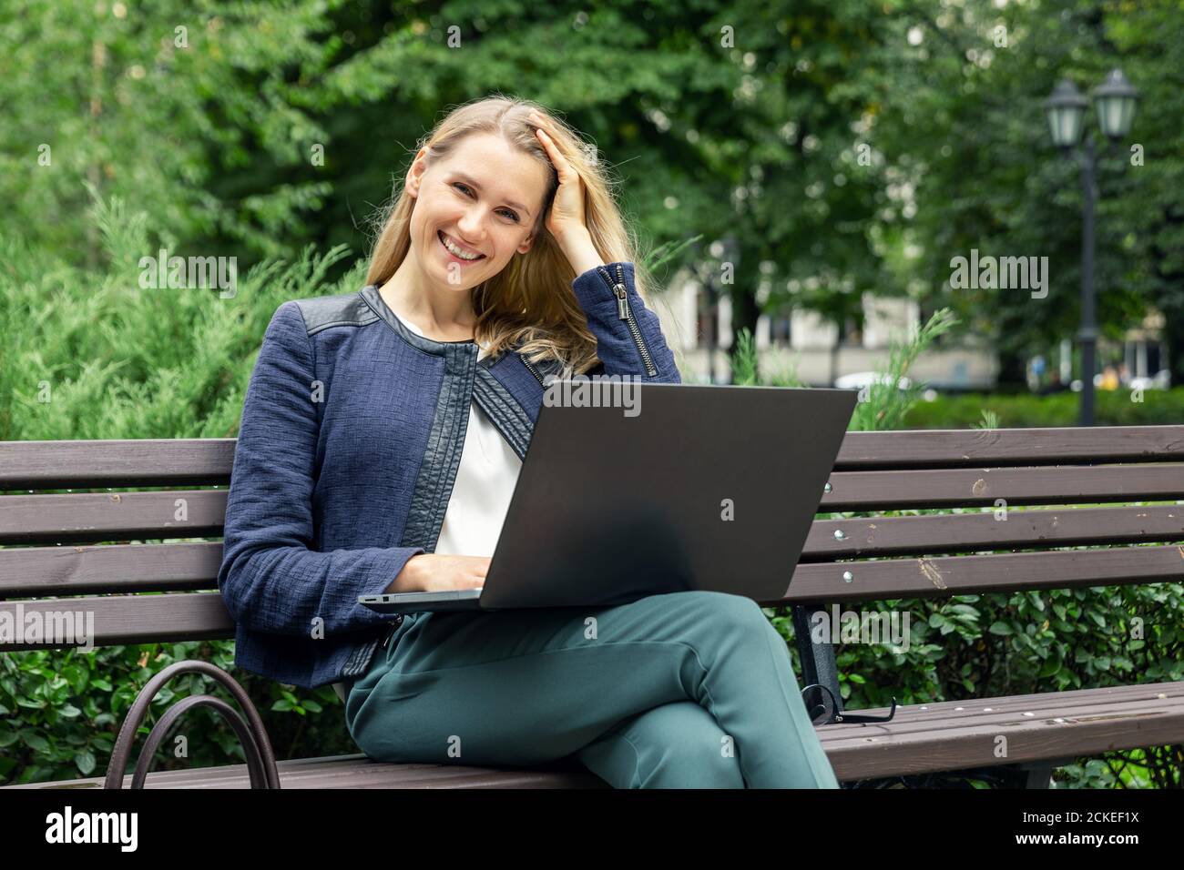 giovane bella donna sorridente che si rilassa sulla panchina nel parco cittadino con computer portatile Foto Stock