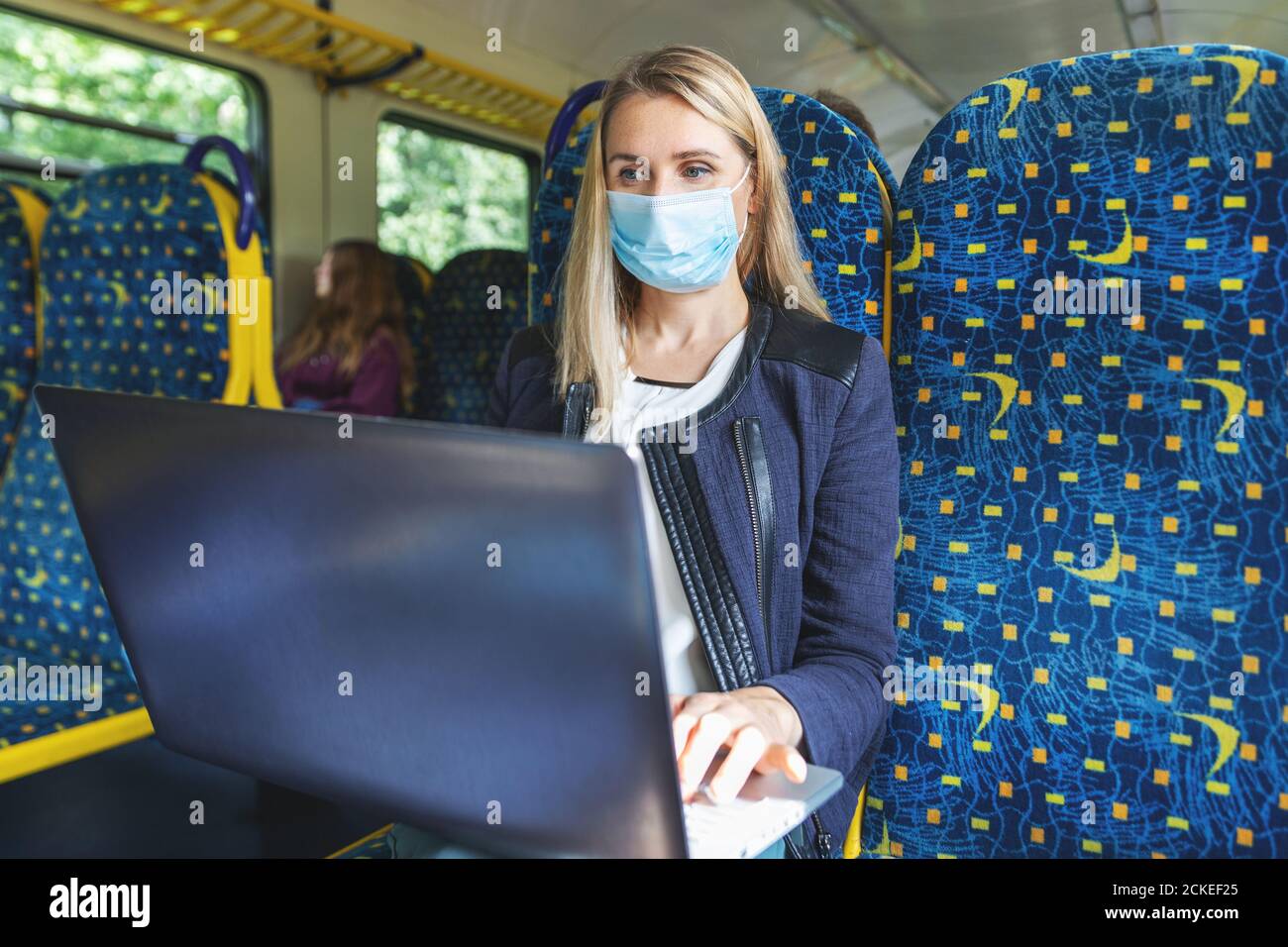 giovane donna con maschera facciale che usa un computer portatile nei trasporti pubblici in treno. pandemia di virus Foto Stock