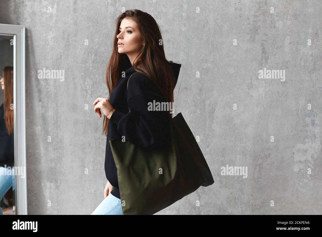 Una giovane donna in felpa nera e jeans blu con una borsa grande sulla  spalla che si pone all'interno Foto stock - Alamy