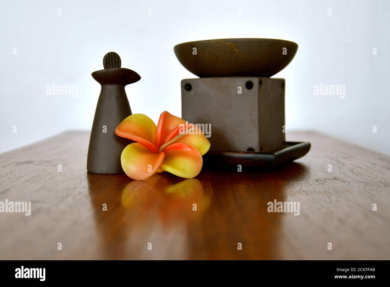 Bruciatore ad olio aromatherapy e bottiglia di argilla in un lussuoso ambiente termale con fiori frangipani. Foto Stock