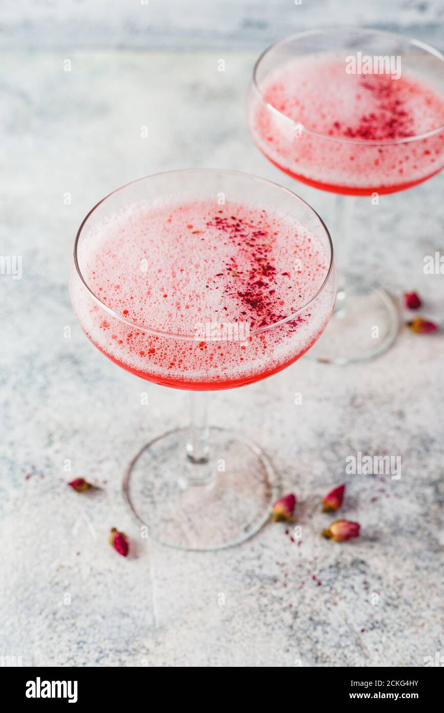 Cocktail alcolico rosa con limonata, champagne o Martini in un bicchiere di champagne, con schiuma e decorato con boccioli di rosa, cocktail come Daiquiri, Foto Stock
