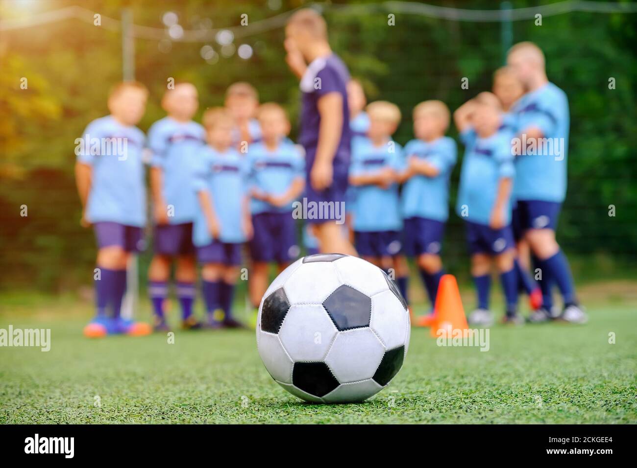 Pallone da calcio e squadra di calcio per bambini offuscati con allenatore il campo Foto Stock