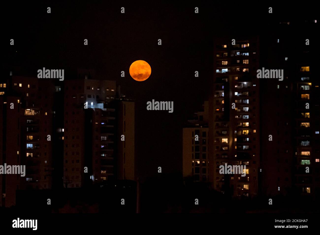 La luna piena arancione sorge su un paesaggio urbano Foto Stock