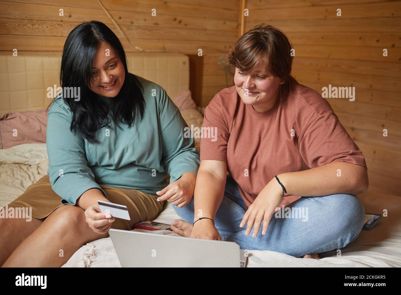 Due donne che usano il laptop per acquistare acquisti online con il credito scheda che si siedono sul letto in camera da letto Foto Stock