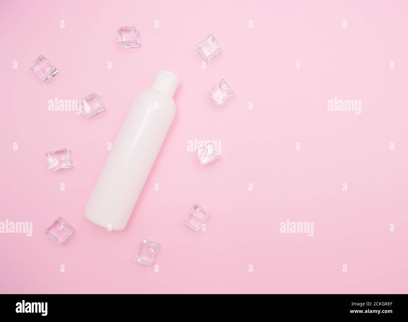 Bottiglia di plastica bianca per shampoo o altri cosmetici. Cubetti di ghiaccio intorno, sfondo rosa, spazio libero per il testo, vista dall'alto. Foto Stock