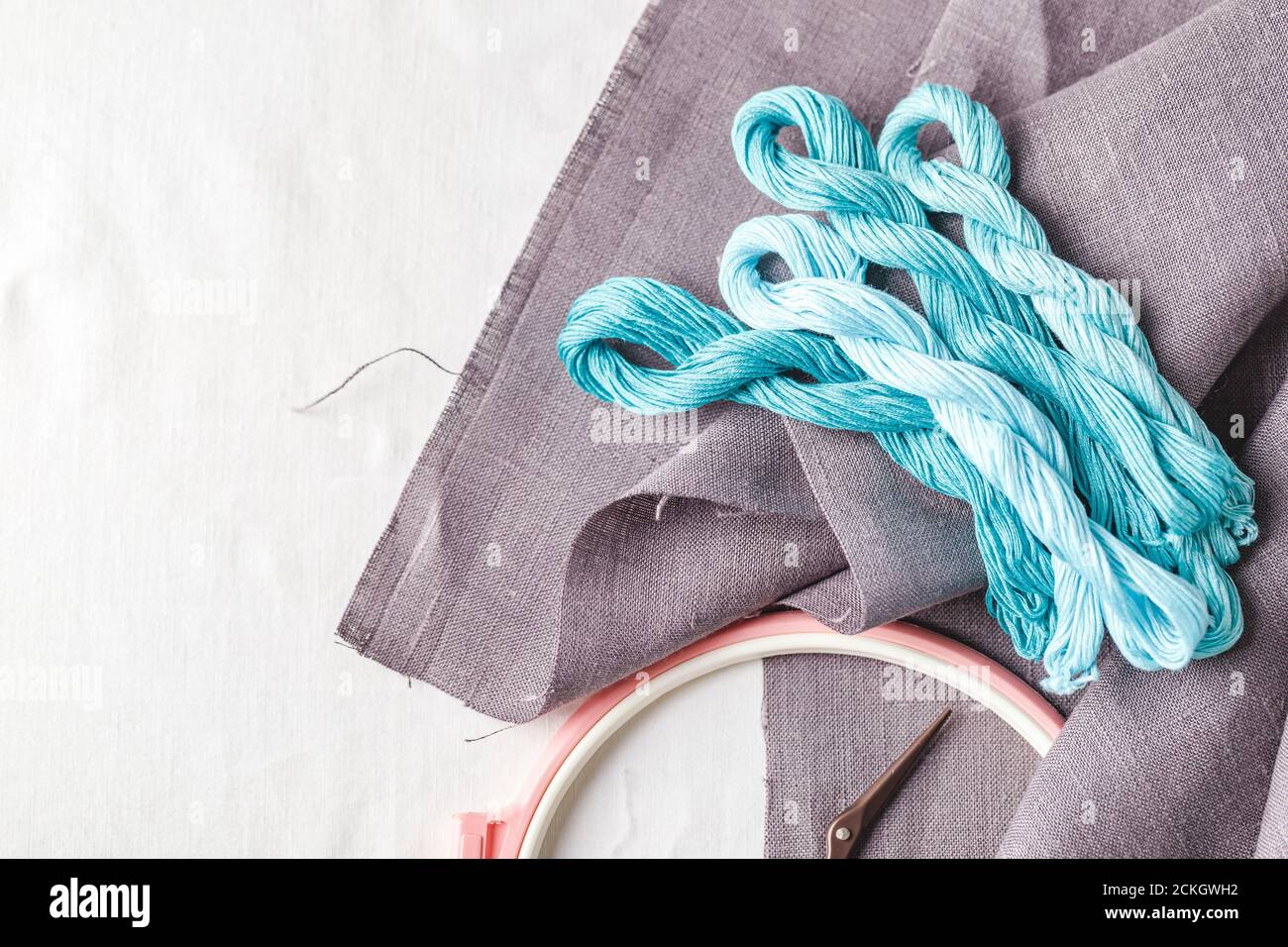 Set per ricamo. Tessuto di lino, motivi per ricamo, cerchi, fili di colore grigio, turchese e blu e aghi. Spazio di copia, vista dall'alto Foto Stock