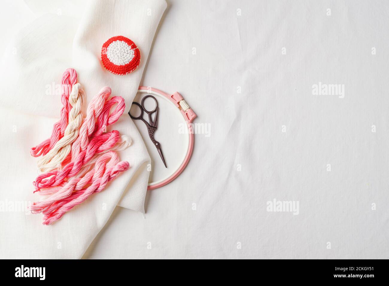 Set per ricamo. Tessuto di lino, motivi per ricamo, cerchi, fili di colore rosa e aghi. Spazio di copia, vista dall'alto Foto Stock