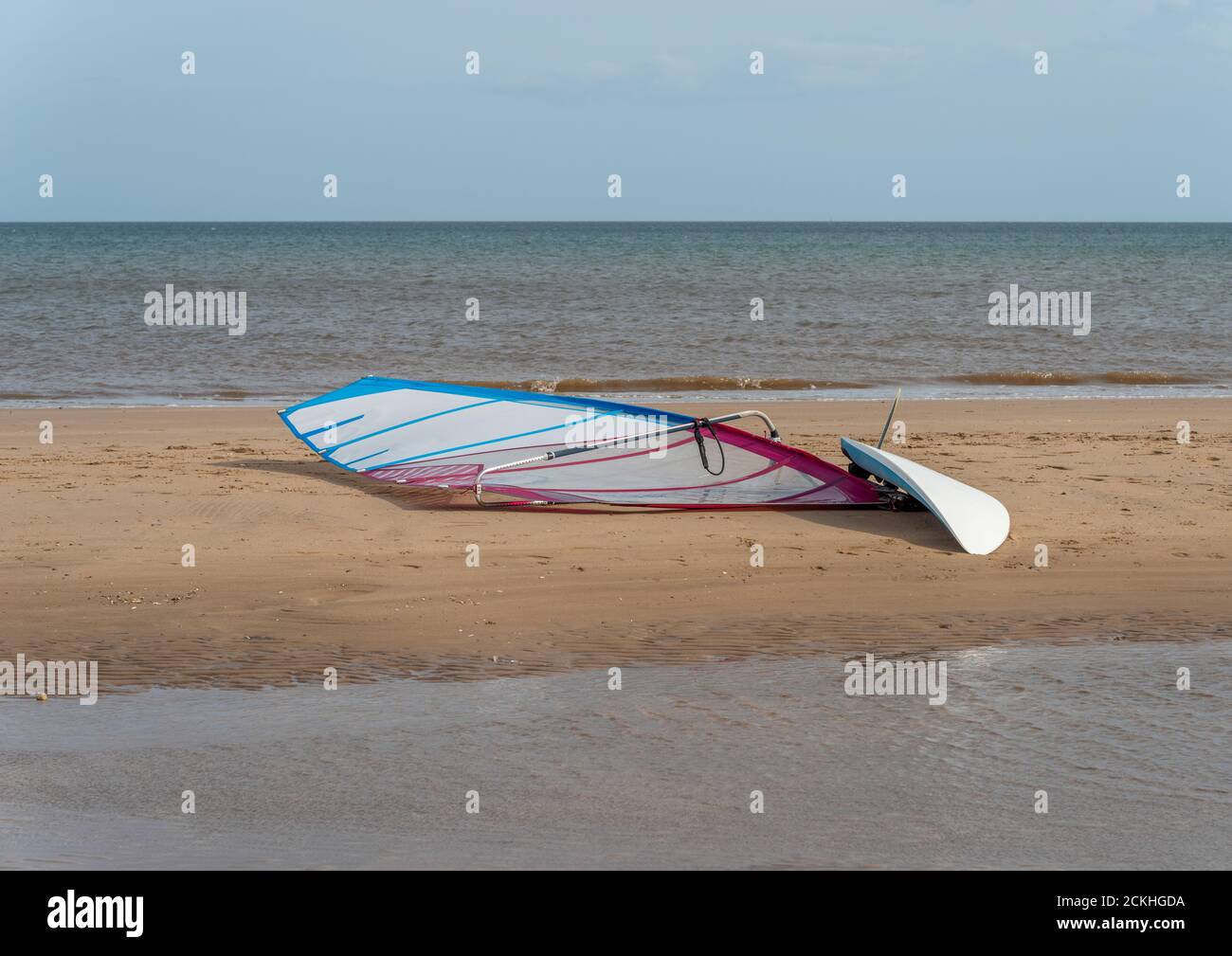 Una singola tavola da windsurf su una spiaggia di sabbia con il mare sullo sfondo Foto Stock