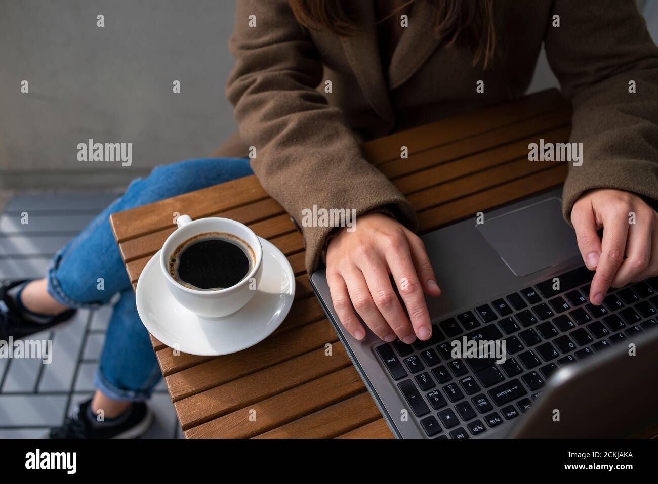 Donna in camice di lana che lavora in un caffè di strada con computer portatile. Tazza di caffè su un tavolo di legno. Foto Stock