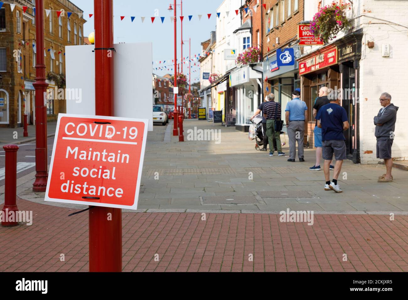 Daventry, Northamptonshire - 16/09/20: Una coda di persone dietro un cartello Covid-19 che ricorda loro di mantenere la distanza sociale. Foto Stock