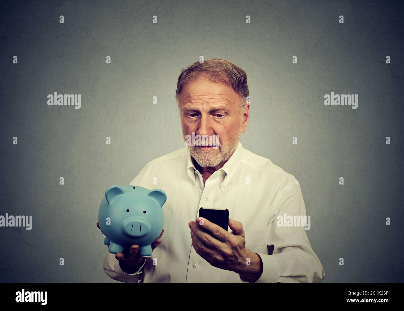 Uomo preoccupato guardando il suo telefono cellulare che tiene una banca piggy Foto Stock