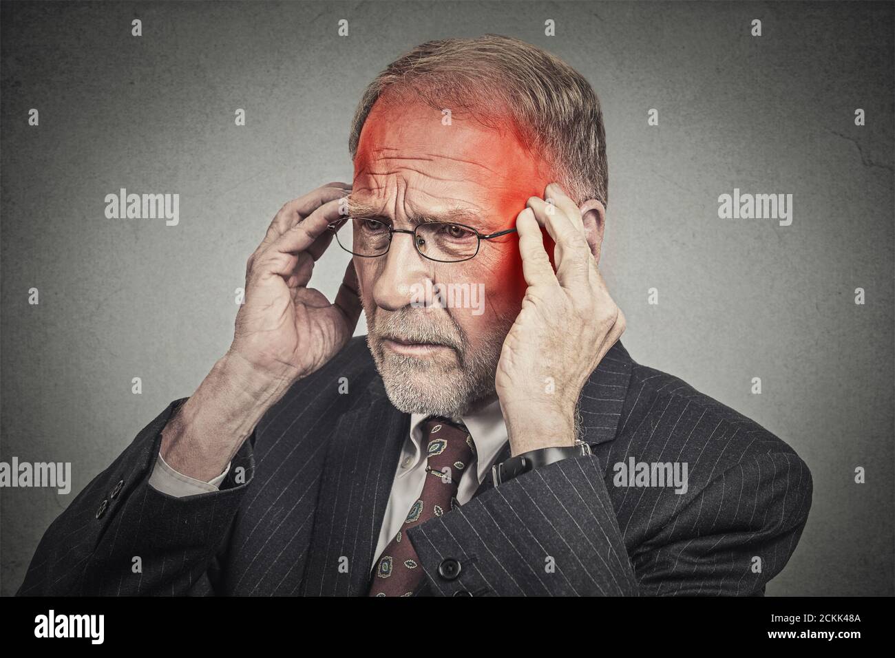 Closeup headshot uomo anziano che soffre di mal di testa mani sulla testa con aree infiammate di colore rosso che guardano verso il basso isolato su sfondo grigio parete. Umano Foto Stock