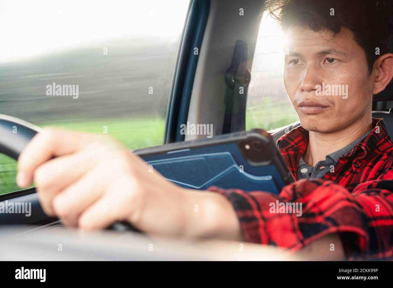 L'uomo usa il tablet o il telefono mentre guida un'auto HIS guardando su un dispositivo e su una strada e sterzando un volante E digitando messaggio e guidando ,pericoloso Foto Stock