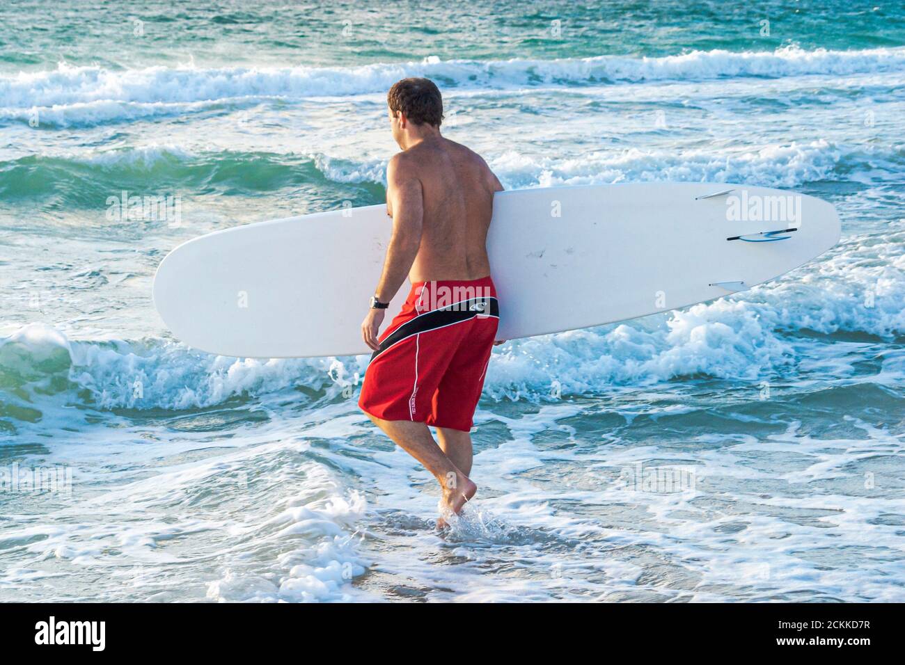 Miami Beach Florida, Atlantic Ocean Shore costa costa costa costa costa mare, surf surf entrare in acqua uomo maschio tenendo onde da surf, persone persona Foto Stock