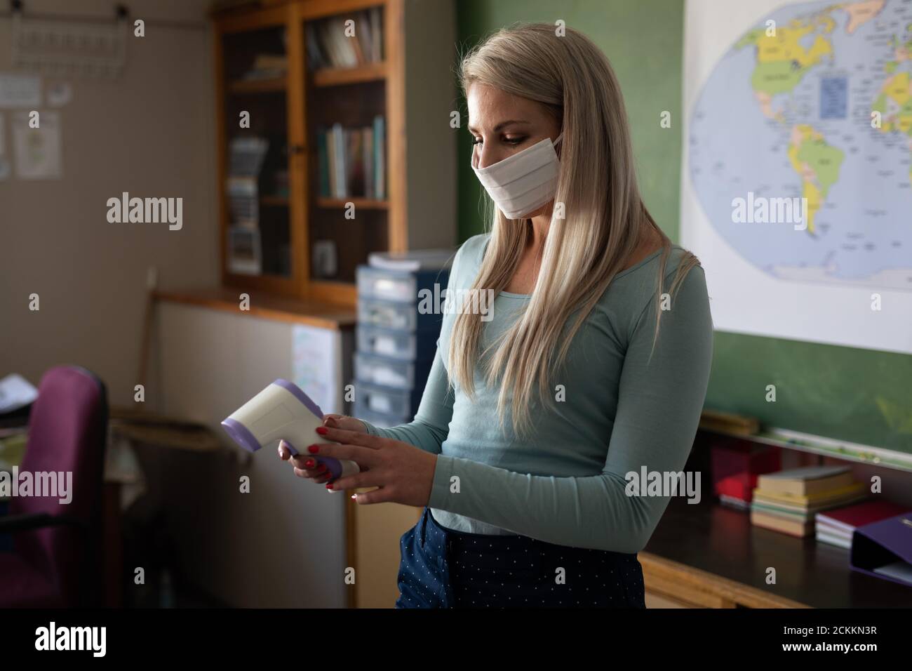 Insegnante femminile che tiene una pistola termica in classe a scuola Foto Stock
