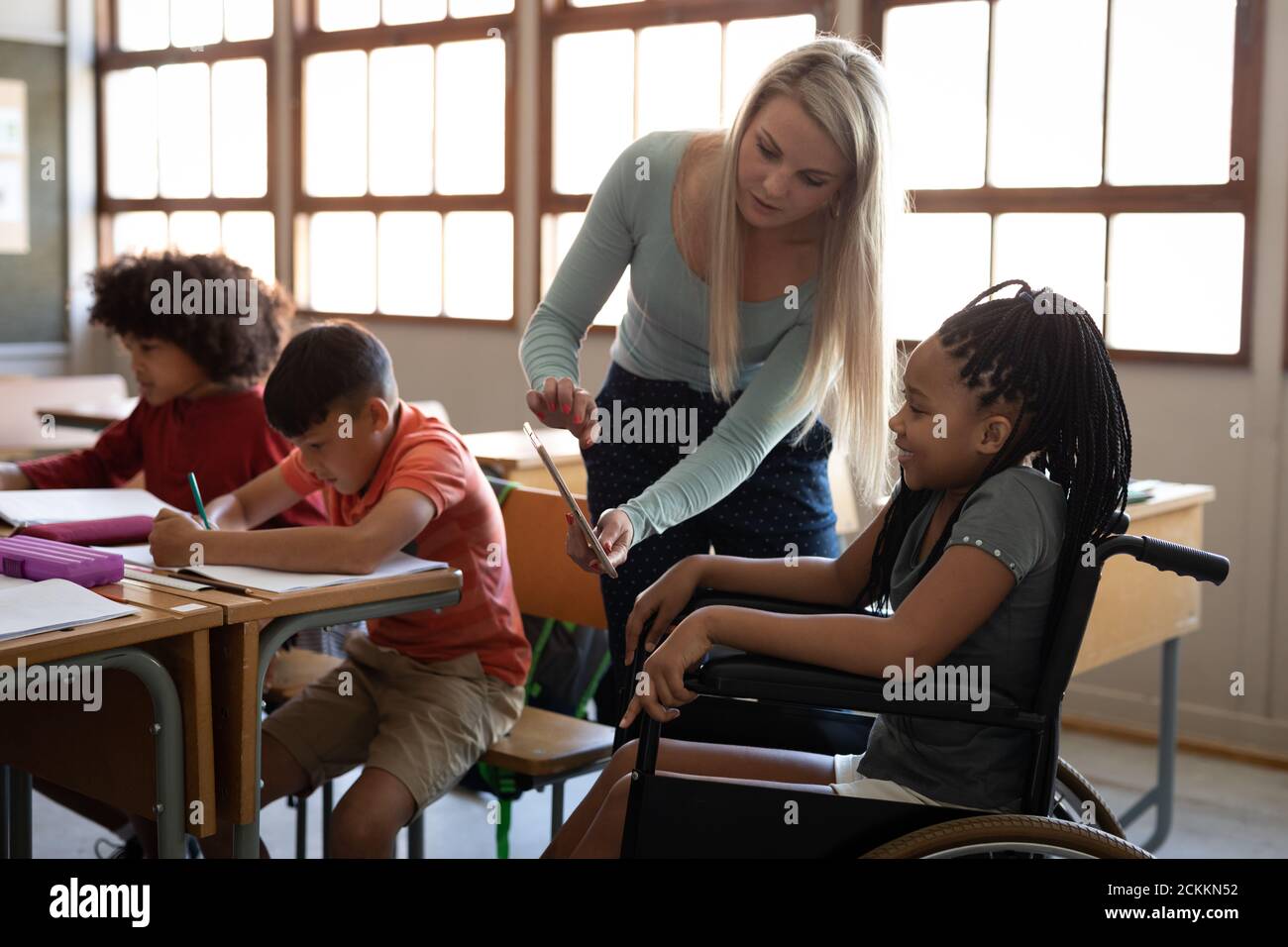 Insegnante di sesso femminile con tablet digitale che insegna una ragazza disable dentro sedia a rotelle a scuola Foto Stock