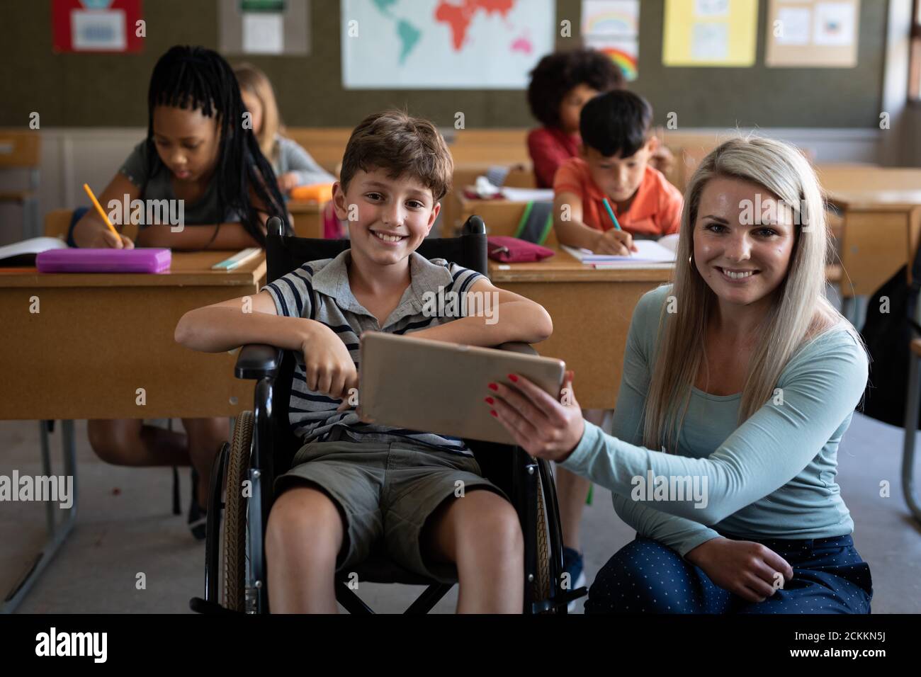 Ritratto di insegnante femminile e ragazzo disabile sorridente mentre si siede in sedia a rotelle in classe Foto Stock