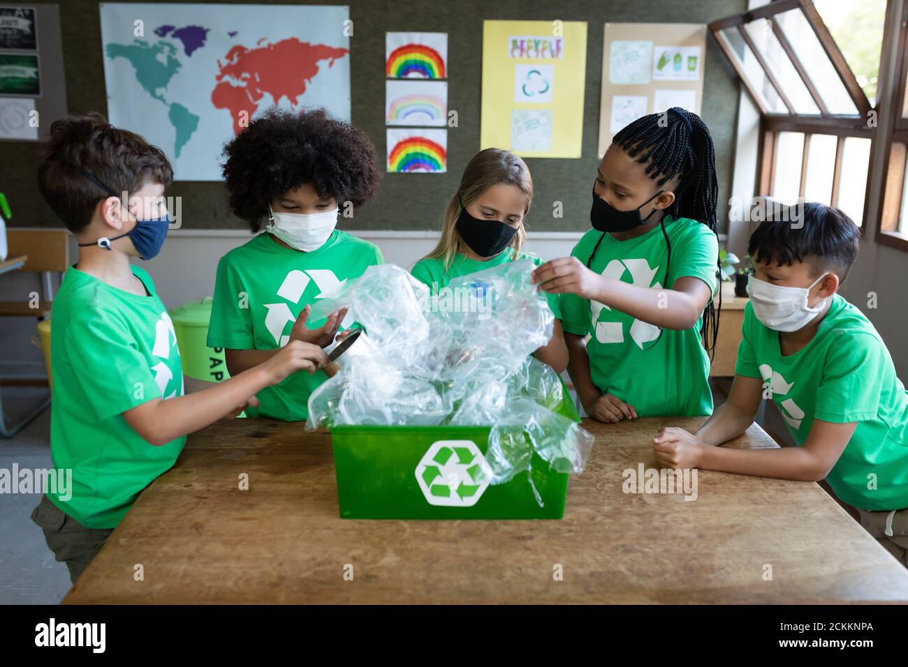 Ritratto di un gruppo di bambini che indossano maschere che toccano la plastica articolo in contenitore di riciclaggio in classe Foto Stock