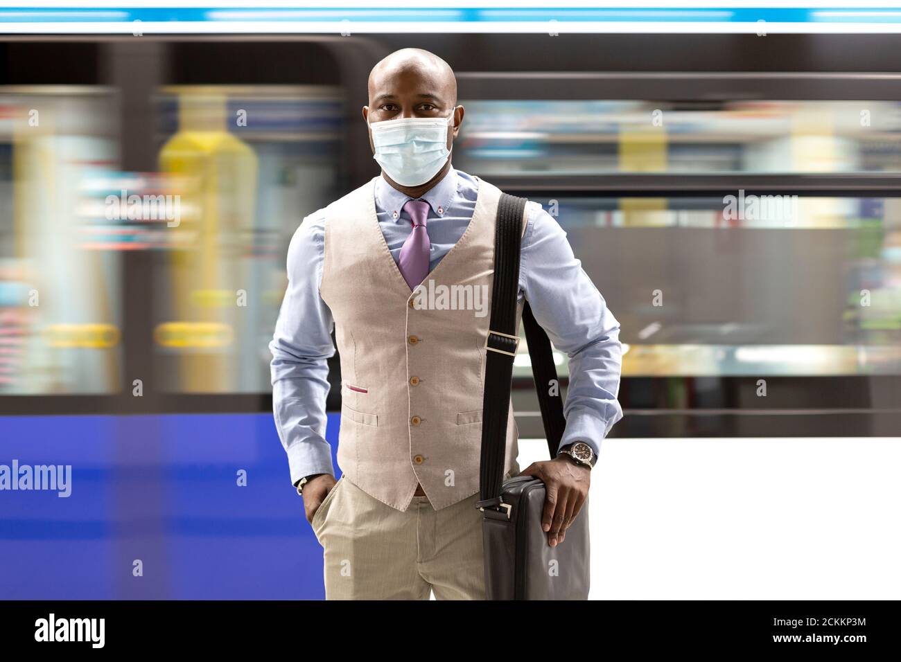 Uomo nero intraprendente che indossa una maschera facciale che cammina vicino a un treno della metropolitana in movimento. Viaggio sicuro durante la pandemia di Covid-19. Foto Stock