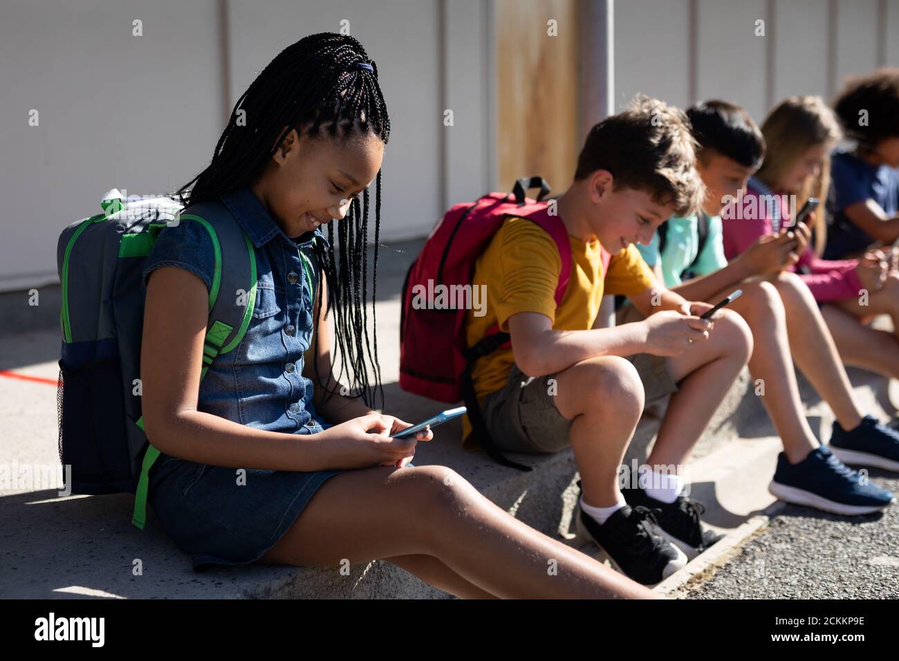 Gruppo di bambini che utilizzano gli smartphone mentre si siedono insieme Foto Stock