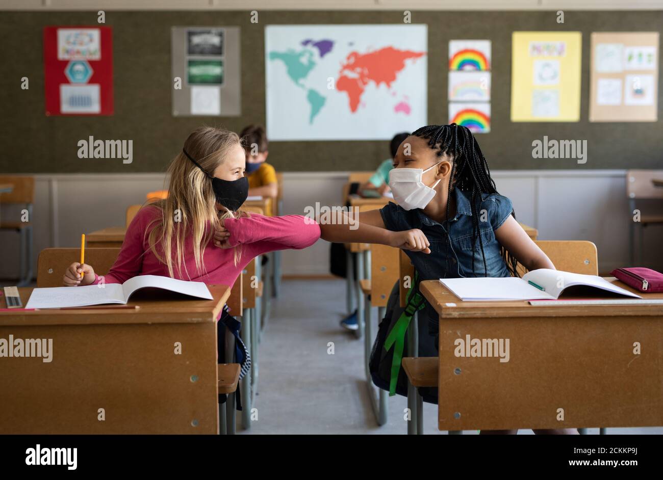 Due ragazze che indossano maschere facciali si salutano a vicenda toccando gomiti a scuola Foto Stock