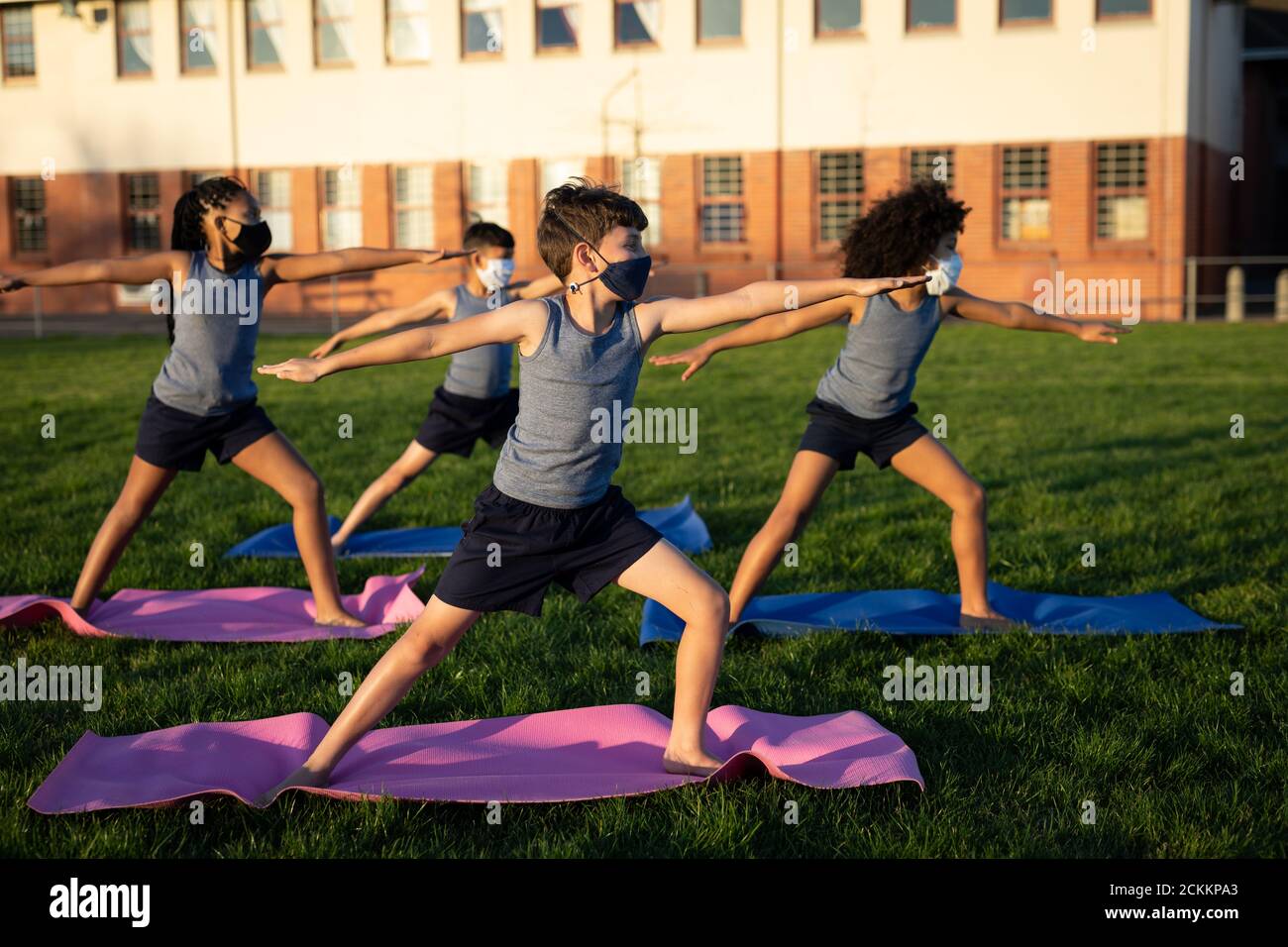 Gruppo di bambini che indossano maschere per il viso che eseguono yoga nella giardino Foto Stock