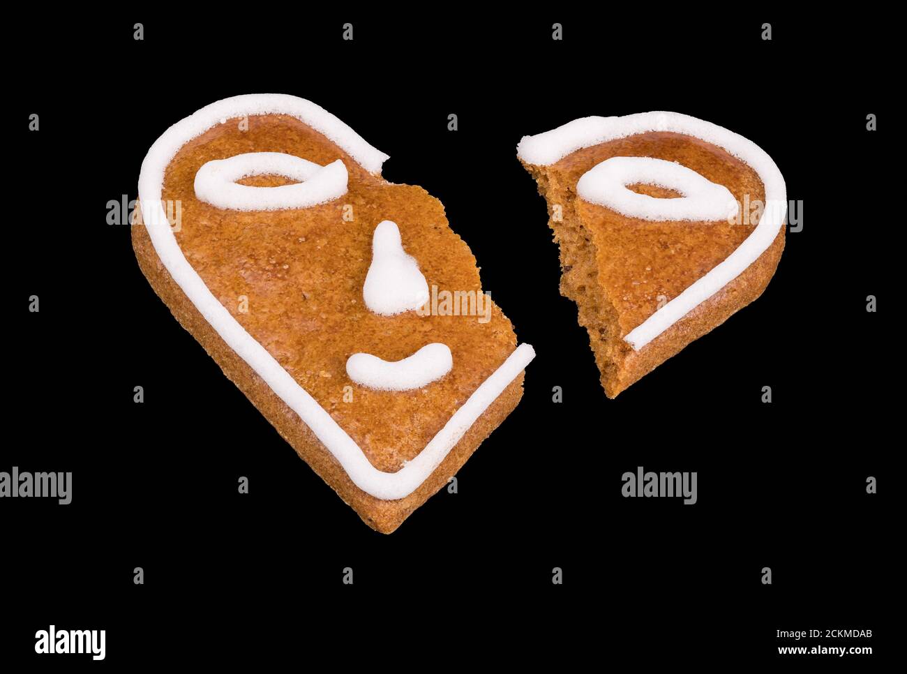 Cuore rotto da pan di zenzero cotto decorato da smiley isolato su uno sfondo nero. Emoticon sorridente diviso in due parti. Fine simbolica dell'amore. Foto Stock