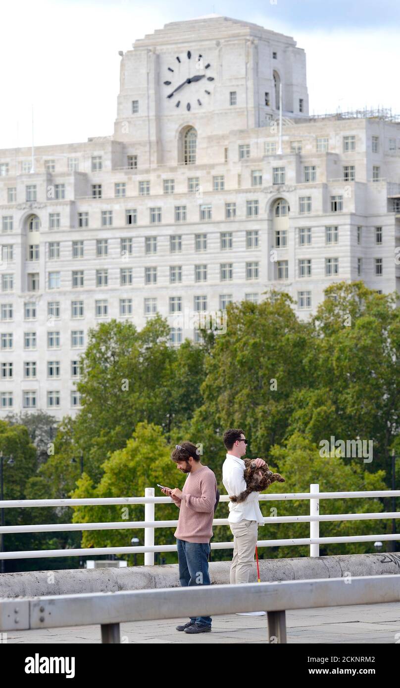 Londra, Inghilterra, Regno Unito. Un uomo sul telefono e un altro che tiene il suo cane (per una foto) sul ponte di Waterloo. Shell Mex House (80 Strand) dietro Foto Stock