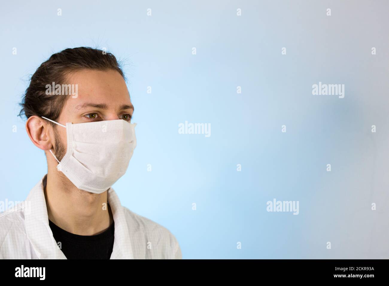 Un maschio adulto vestito con un camice da laboratorio bianco con una maschera protettiva sul viso. Pronto a lavorare in un ambiente pulito o in laboratorio Foto Stock