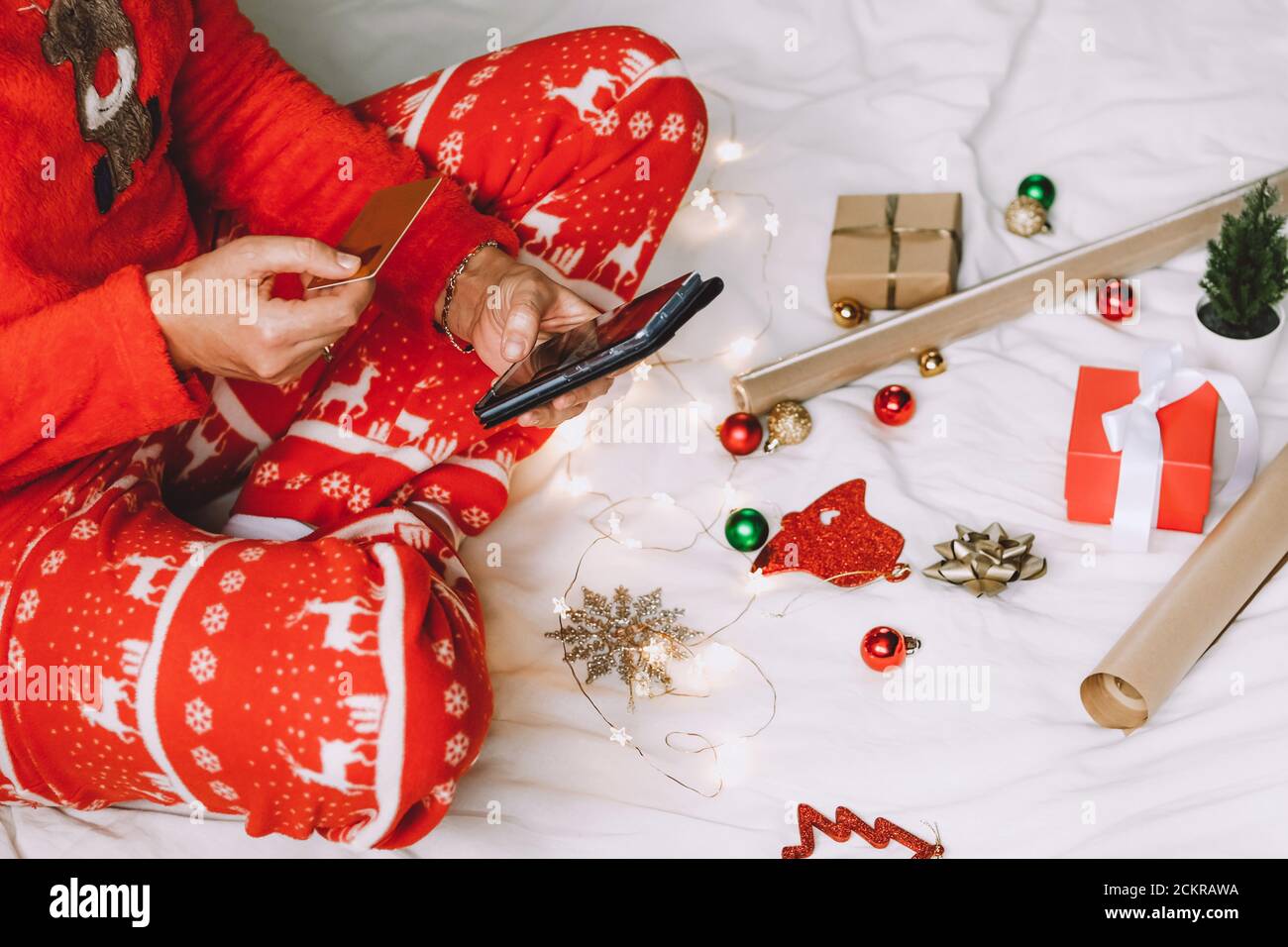 Donna che acquista in linea per i regali di Natale. Immagine ritagliata di una ragazza con telefono cellulare e carta di credito che prepara i regali di vacanza. Foto Stock