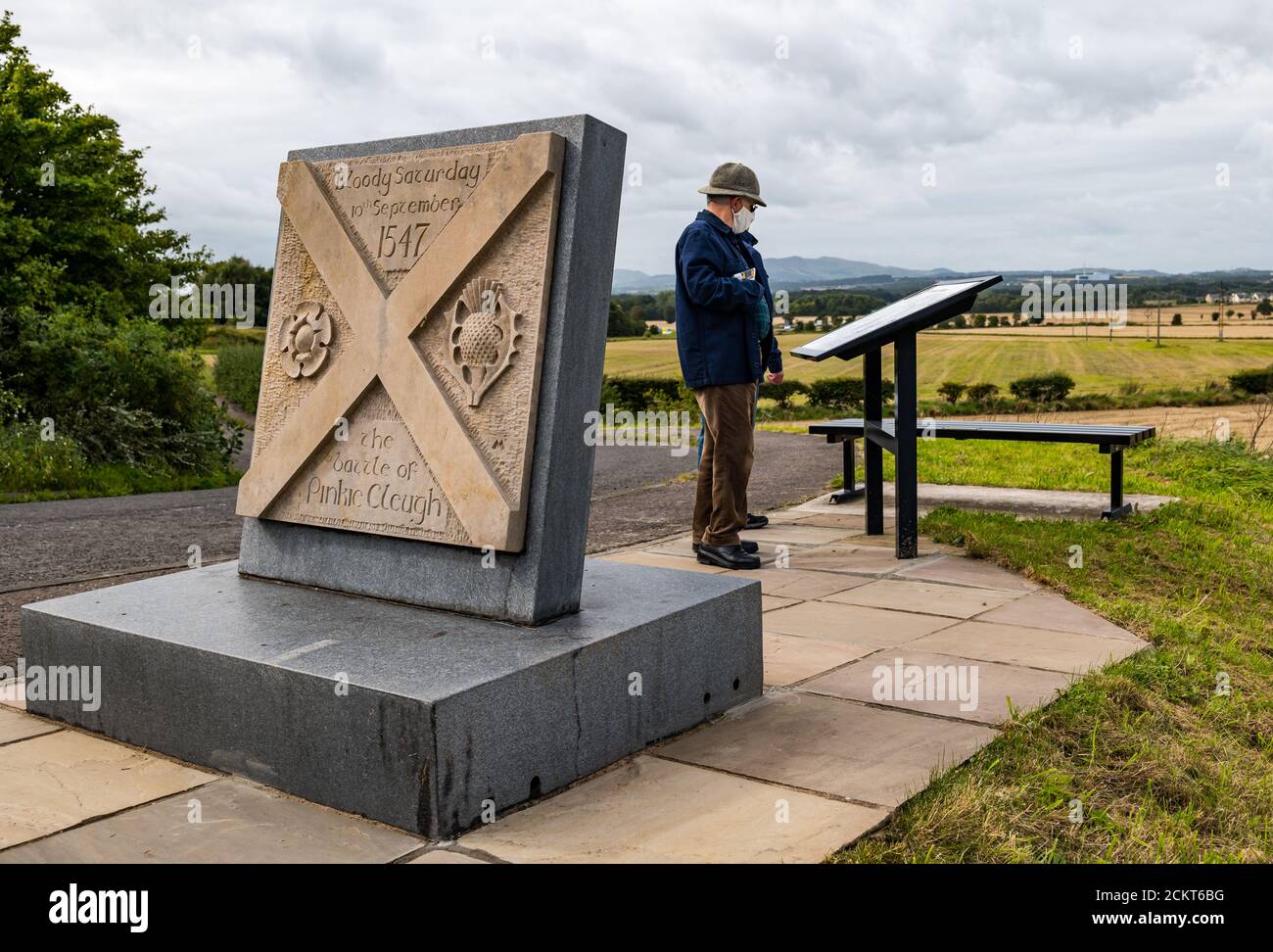 Un uomo che indossa una maschera facciale legge il bordo di informazioni del percorso di battaglia, memoriale della battaglia di Pinkie Cleugh, East Lothian, Scozia, Regno Unito Foto Stock