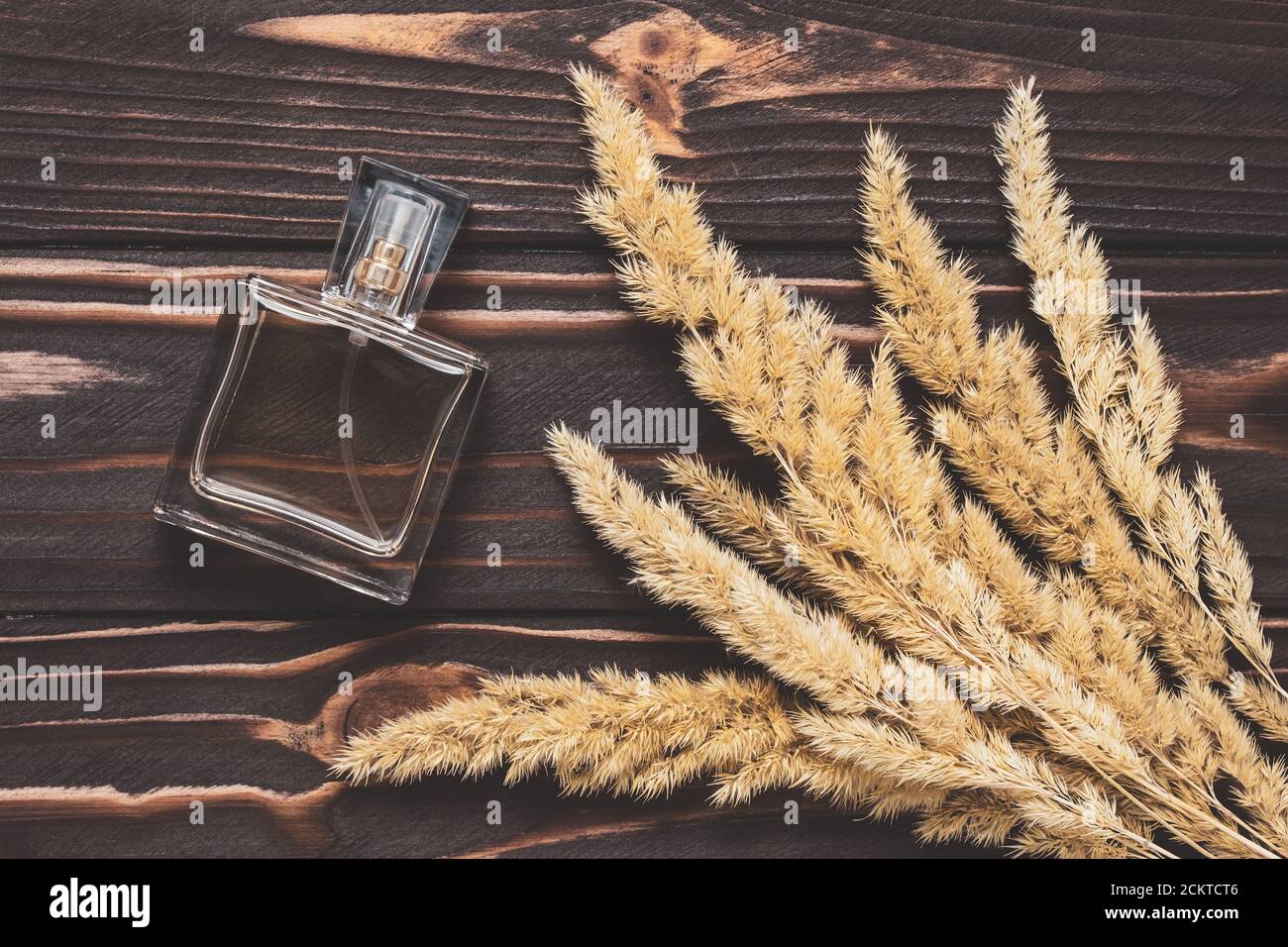 Profumo in una bottiglia di vetro su tavole di legno marrone scuro e orecchie gialle secche. Acqua di toletta, ancora vita. Composizione piatta, design decorativo Foto Stock