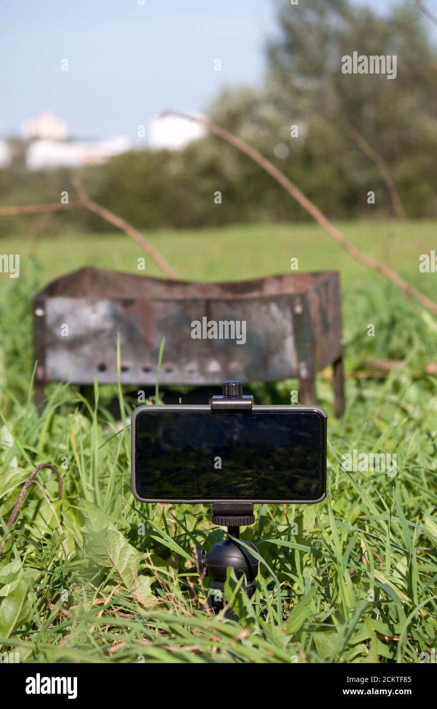 Grigliate in metallo tra l'erba verde nel prato. Davanti a lui c'è uno smartphone su un treppiede. Scattare un picnic. Foto Stock