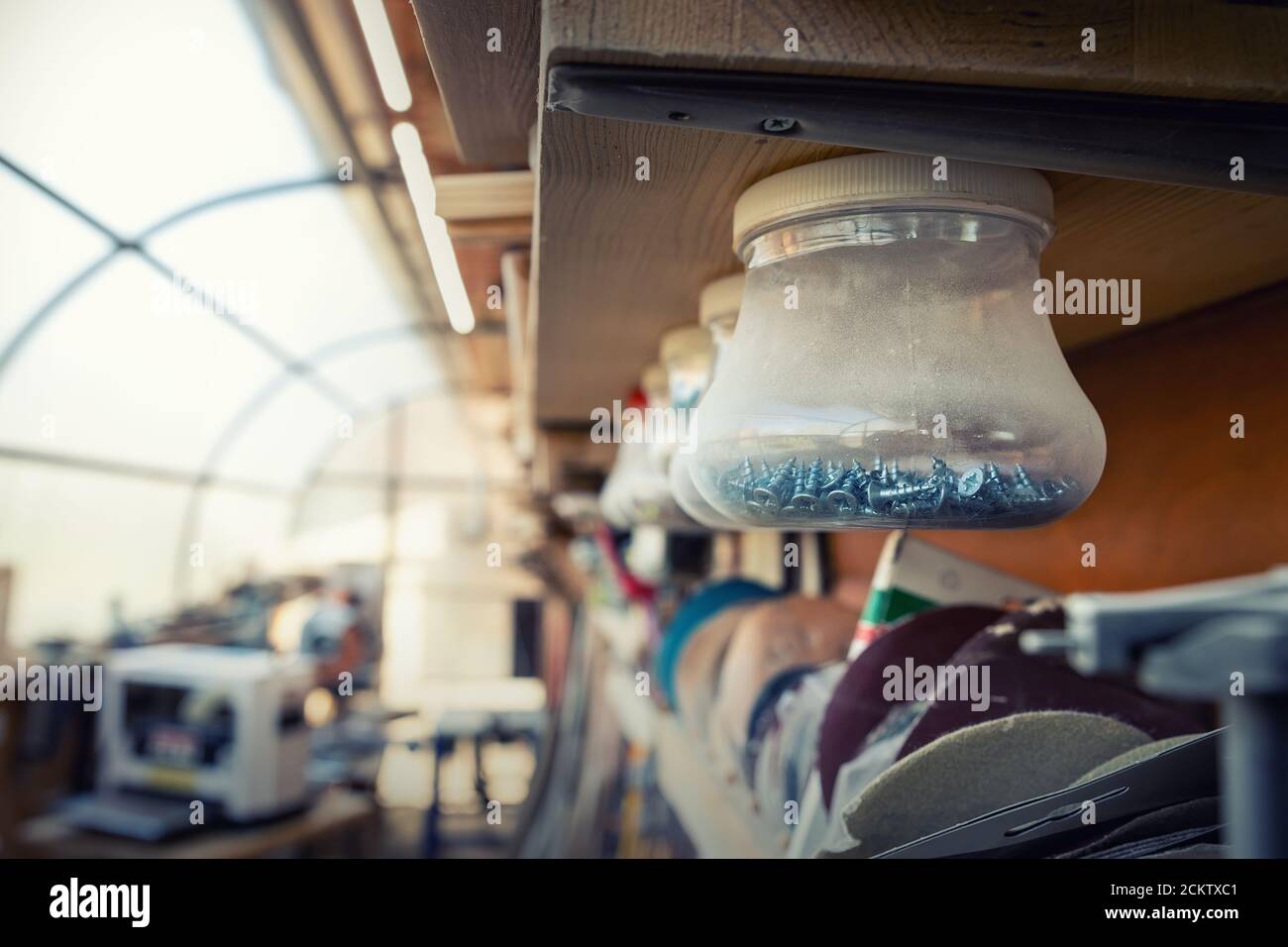 Interni di officina in legno con molti attrezzi e attrezzature differenti. Vasi in plastica con molte viti diverse chiodi sospesi su scaffale per Foto Stock