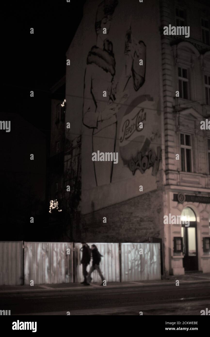 Foto di strada - Scene notturne Praga strade, Repubblica Ceca, Europa - una coppia a piedi oltre un grande edificio della città con immagine Pepsi Cola sul muro Foto Stock