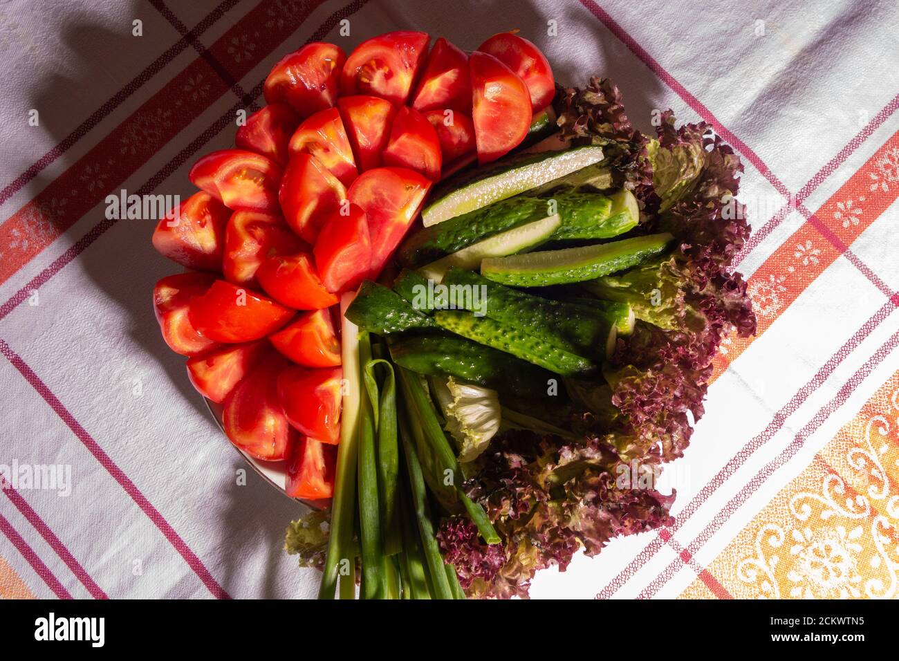 Semplice cibo estivo - pomodori, cetrioli, cipolle, lattuga in un piatto su un tavolo con una tovaglia. Cibo vegetariano. Foto Stock