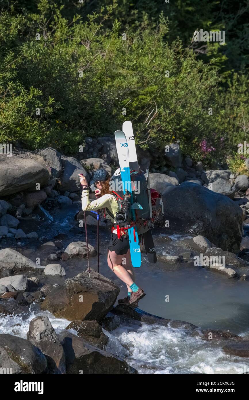 Donna di montagna di sci che attraversa un torrente di meltwater glaciale che esce dal ghiacciaio Coleman e dalla dorsale di Heliotrope sulle pendici del monte Baker, il monte Baker-Sn Foto Stock