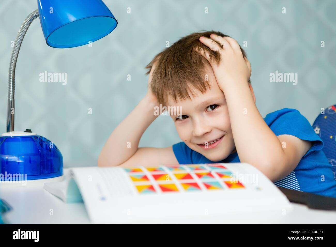 Un ragazzo di scuola tiene la testa e legge un libro Foto Stock