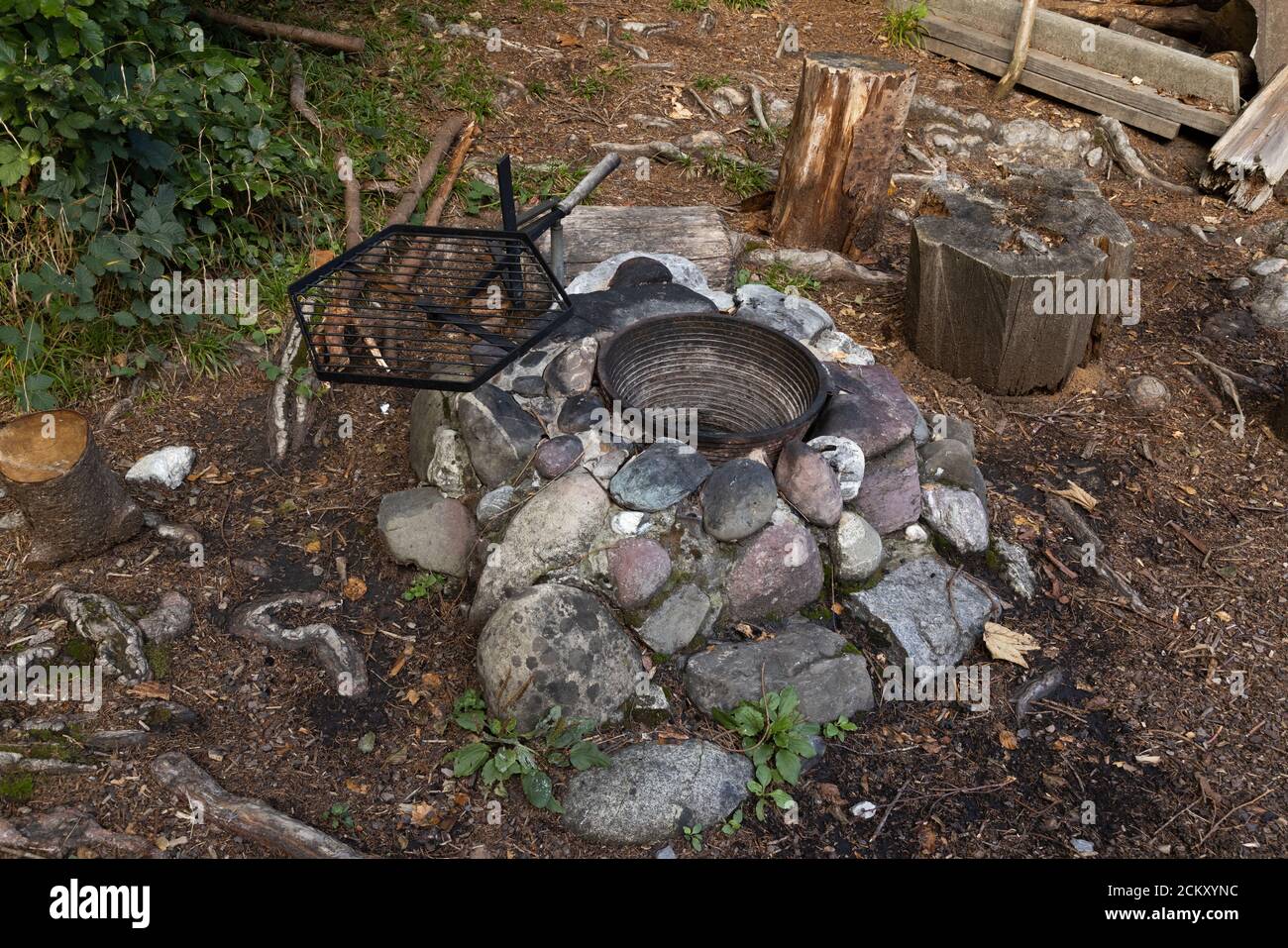 camino con vaso di ottone vuoto e griglia nera vuota tra pietre grigie e pavimento di foresta marrone, caminetti offrono agli escursionisti un posto di cottura per preparare il th Foto Stock