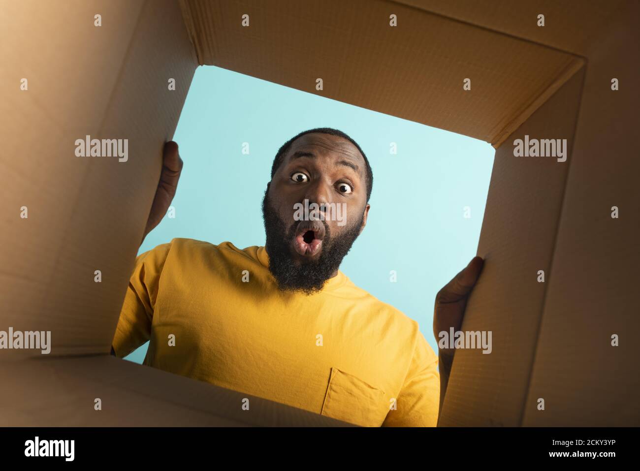 Happy Boy riceve un pacchetto dall'ordine del negozio online. Espressione felice e sorpresa. Sfondo blu. Foto Stock