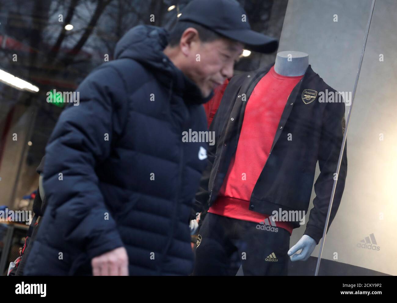 Un uomo cammina davanti a una vetrina Adidas dove un modello è vestito in abiti  sportivi con il logo della squadra di calcio inglese Arsenal, a Pechino,  Cina 16 dicembre 2019. REUTERS/Jason